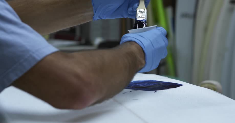 A man with gloves painting a surfboard with a paint brush