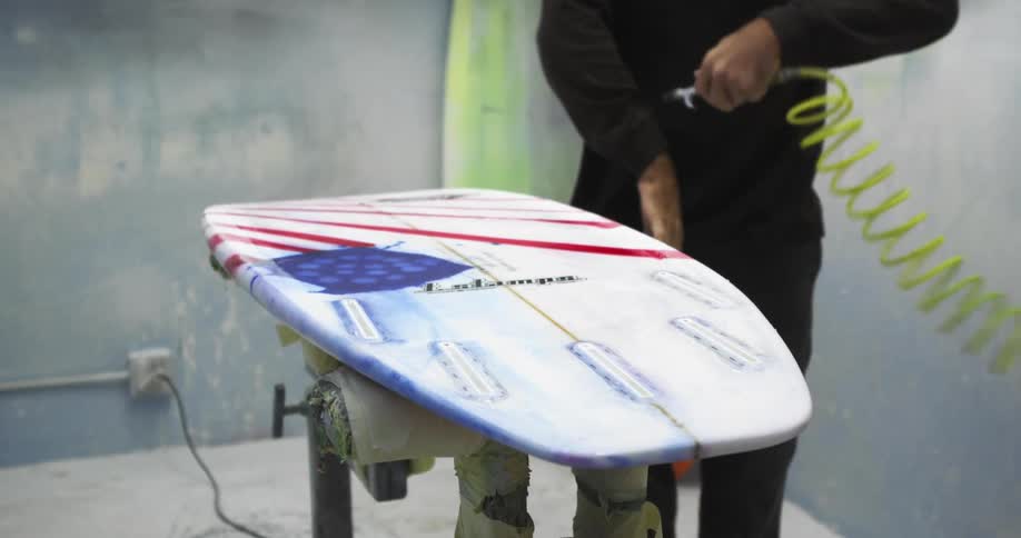 A man uses an air hose to clean off a board he is working on then uses it to spray dust off himself