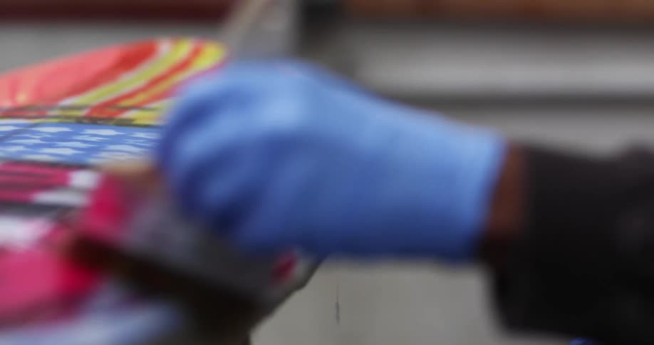 A person wearing latex gloves covers a surfboard with varnish using a brush