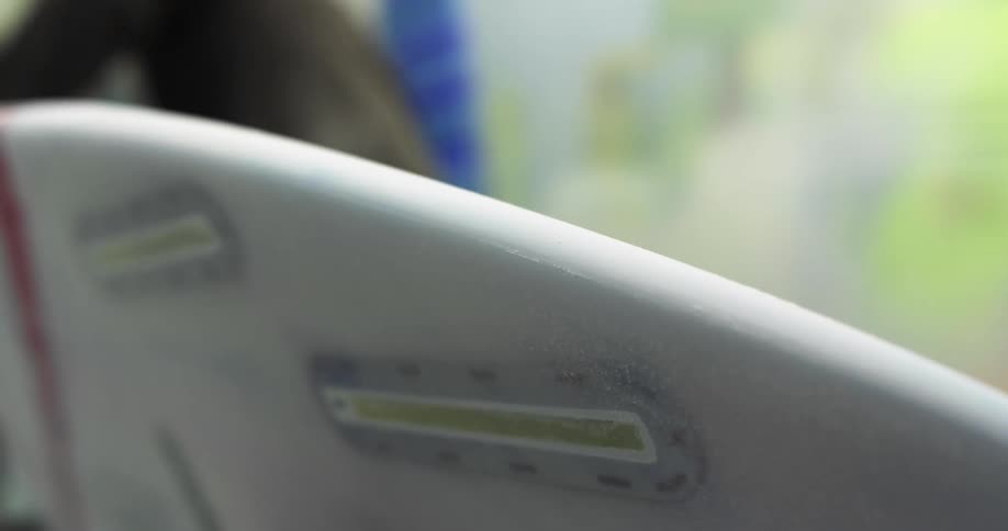 Man wearing gloves polishing and smoothing the sides of an incomplete surfboard indoors