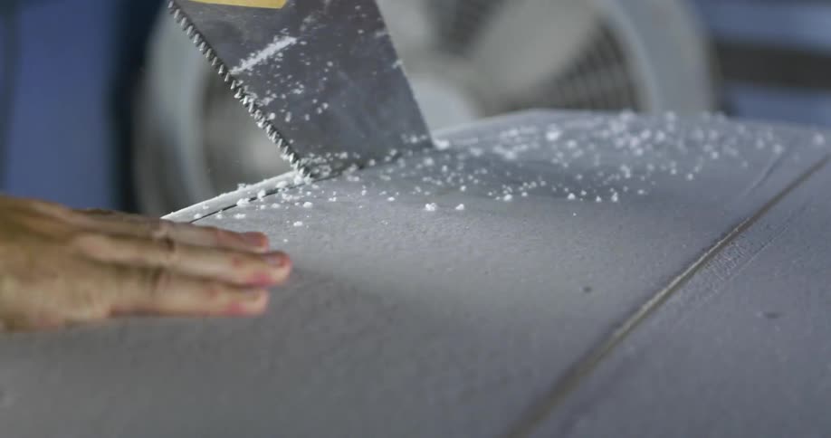 Sawing edge off a surfboard with a hand saw