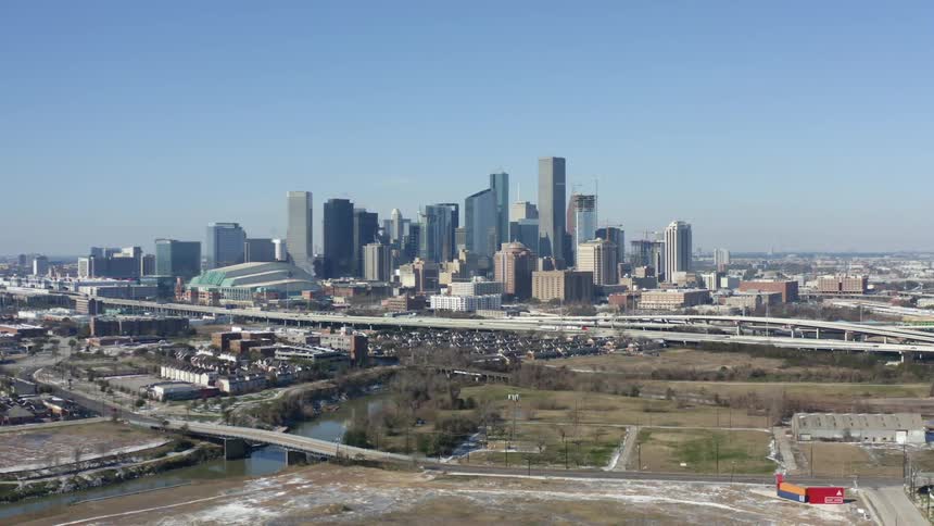 Aerial view of high rise buildings in the distance on a skyline and a highway in a city where cars are driving by during the day