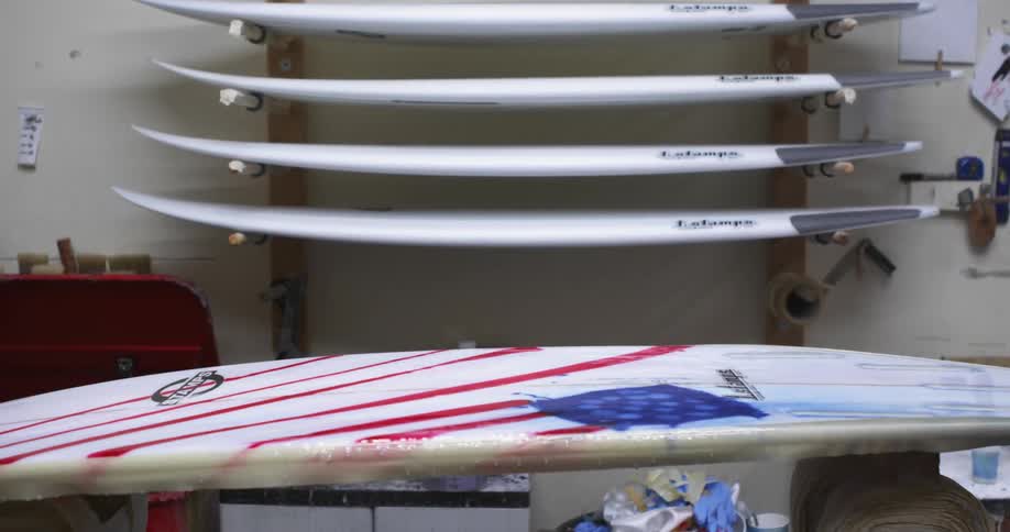 A surfboard in a room with a rack of surfboards and a wall in the background