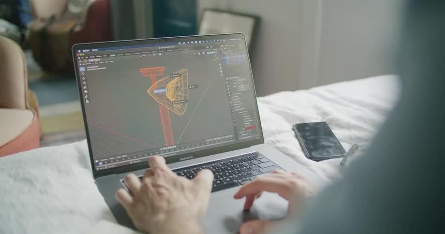 A man sitting on a bed working on a laptop with his phone beside it