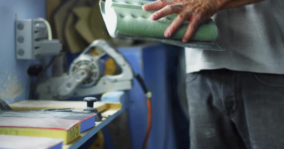 A man holding dusty sandpaper in a workshop