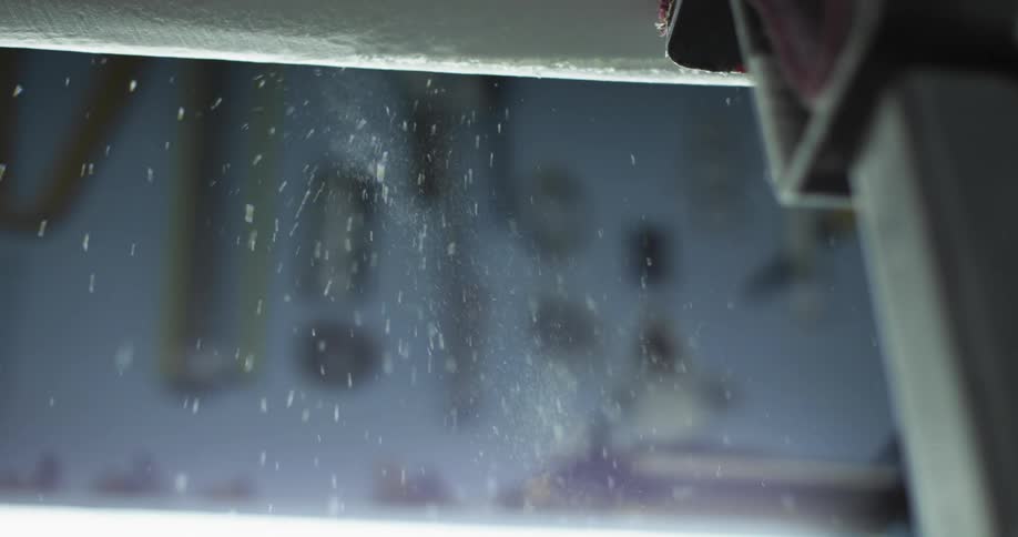 A silver hand held saw cuts down the edge of a piece of foam