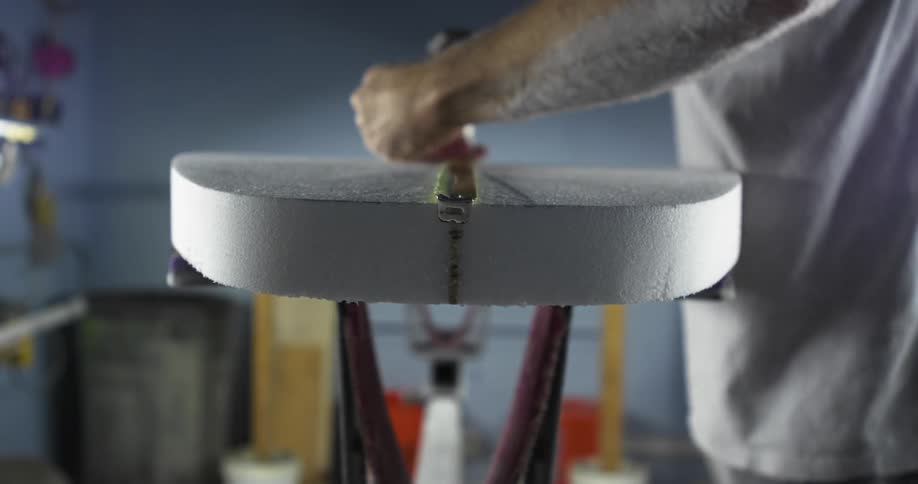 A person drawing markings on the surface of a surfboard inside a workshop