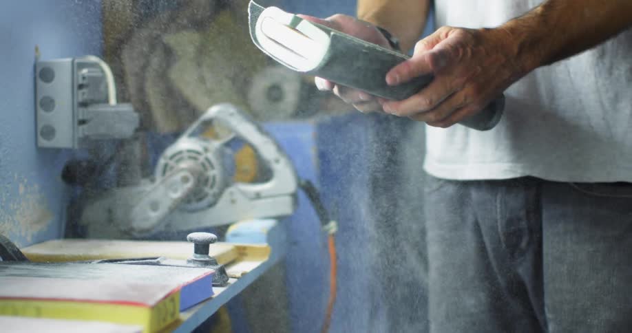 Sawdust goes flying as a man picks up a large sponge sitting next to a saw in his workshop