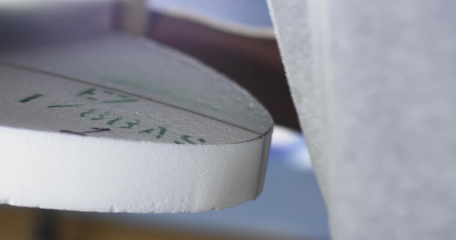 A person in a room sanding a surfboard with sand paper and a board
