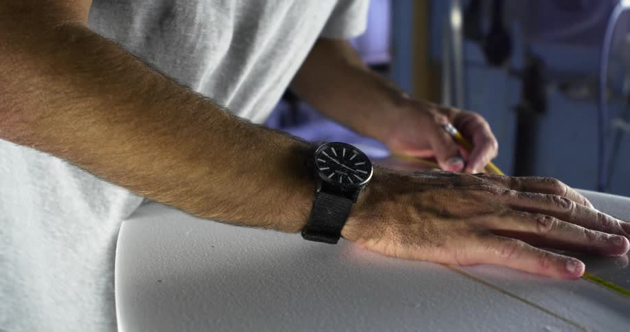 A man takes measurements and draws lines on a surfboard
