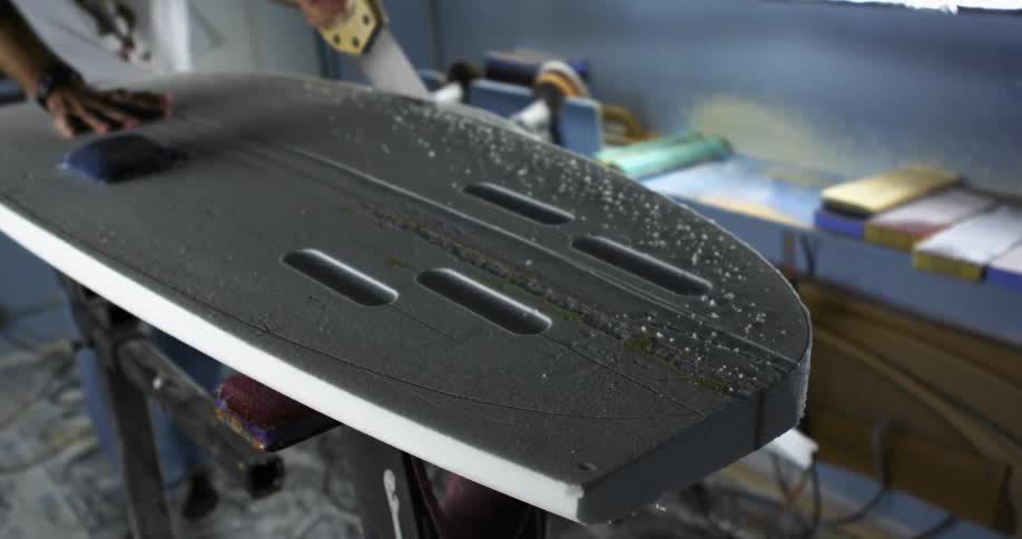 A person in a room cutting out a surfboard with a saw