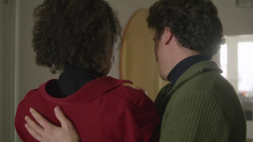 A husband hugs his wife and they watch a pregnancy test and then smile and embrace again indoors at daytime