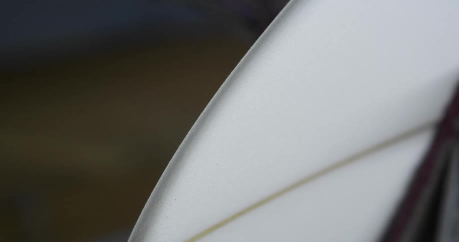 A man sanding the surface of a surfboard in a workshop