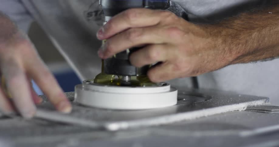 A person usses a router power tool to perforate a surfboard