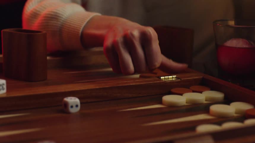 A person in a room sitting at a table playing a board game with dice