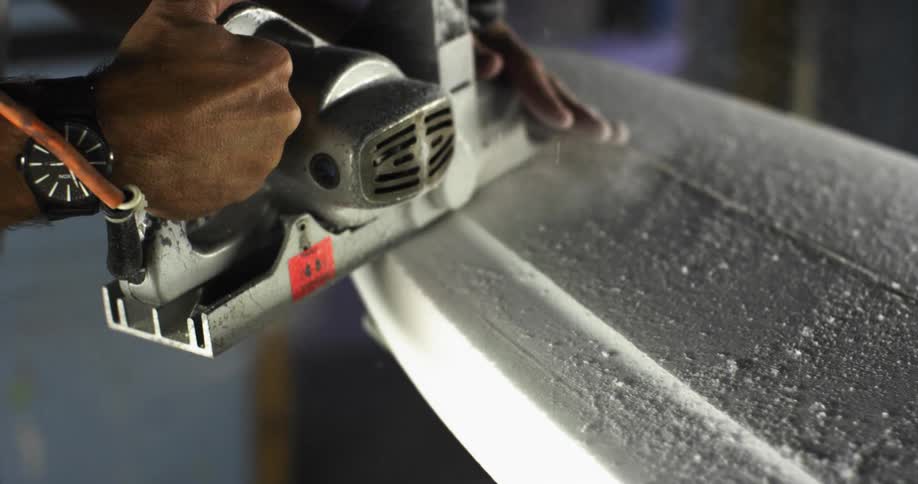 A person with an electric sander sanding a surfboard