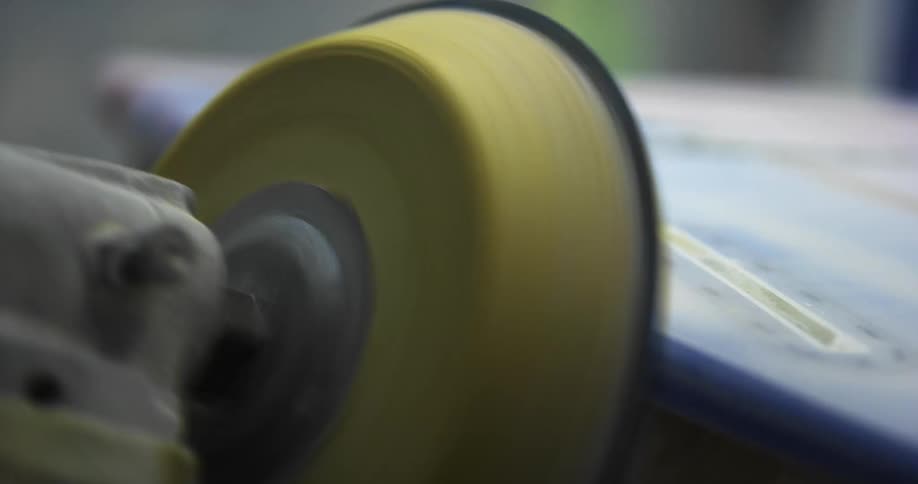 A person uses a power tool to sand the edges of a surfboard inside a workshop