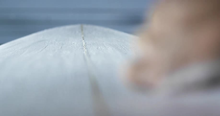 A man smooths the surface of a surfboard with a tool indoors