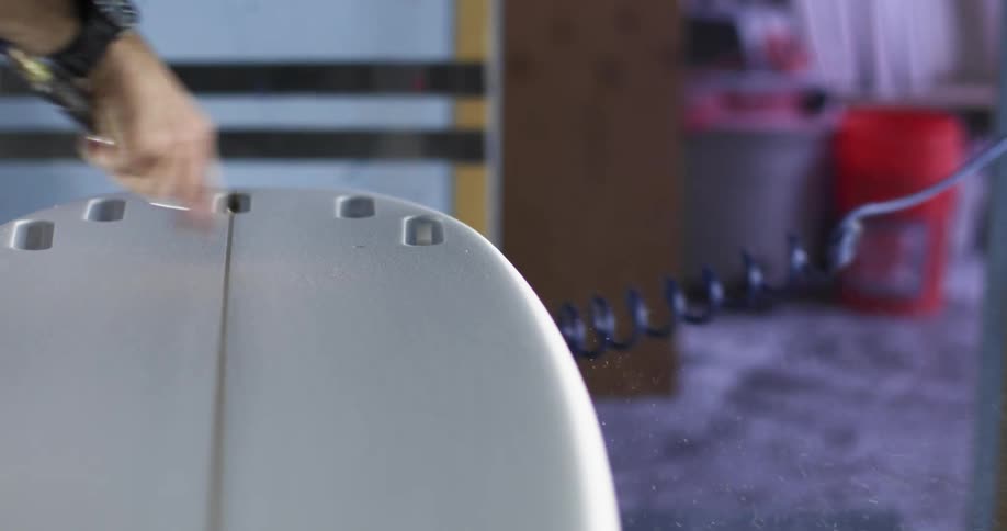 A man uses compressed air to clear the surface of a surfboard from debris