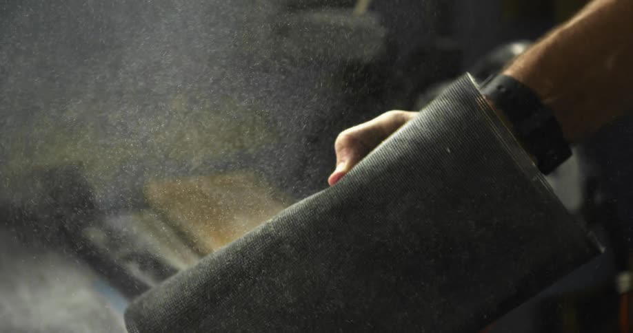 Man dusts fabric covering in workshop near machinery
