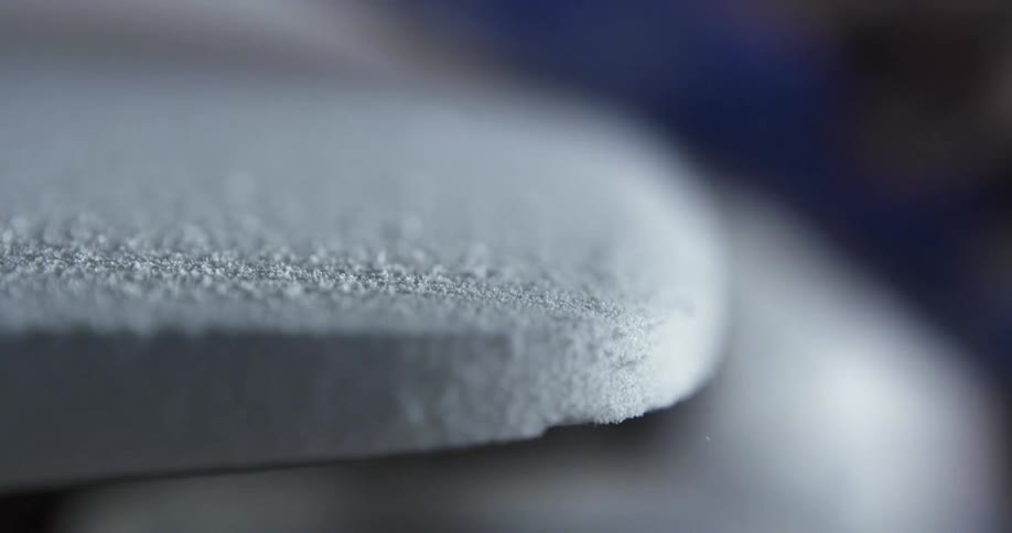 A man sanding the surface of a surfboard by hand in a workshop