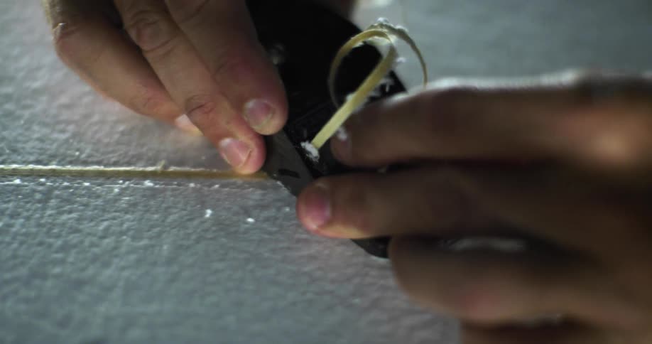A man cutting a ribbon of material from the surface of a surfboard
