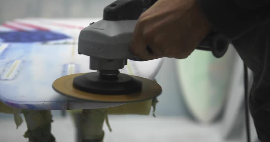 A man uses a sander to smooth the surface of a surfboard painted red white and blue