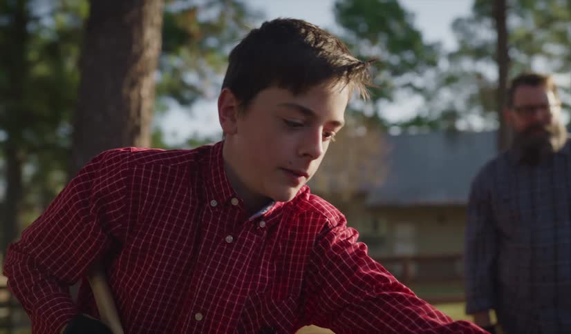 Son with red shirt cuts wood with ax next to his father
