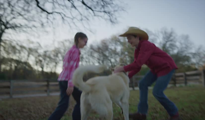 Boy wearing hat and red shirt and girl with pink shirt play with labrador retriever