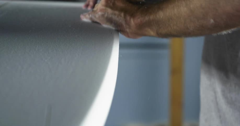 A man sanding the edge of a surfboard in a workshop
