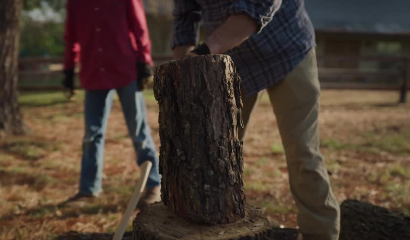Father and son setting up a piece of wood outside on a chopping block in a fence enclosure during the day