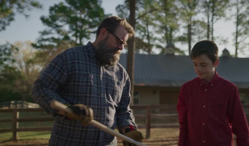 A boy retrieves an ax from the bed of a truck and carries it over to a man who carefully examines the blade