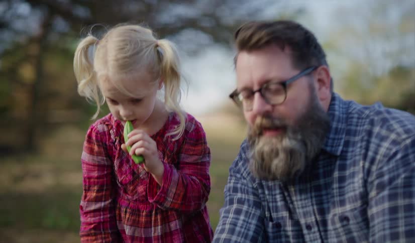 A man with glasses talking to a girl in a garden with a vegetable in her hand