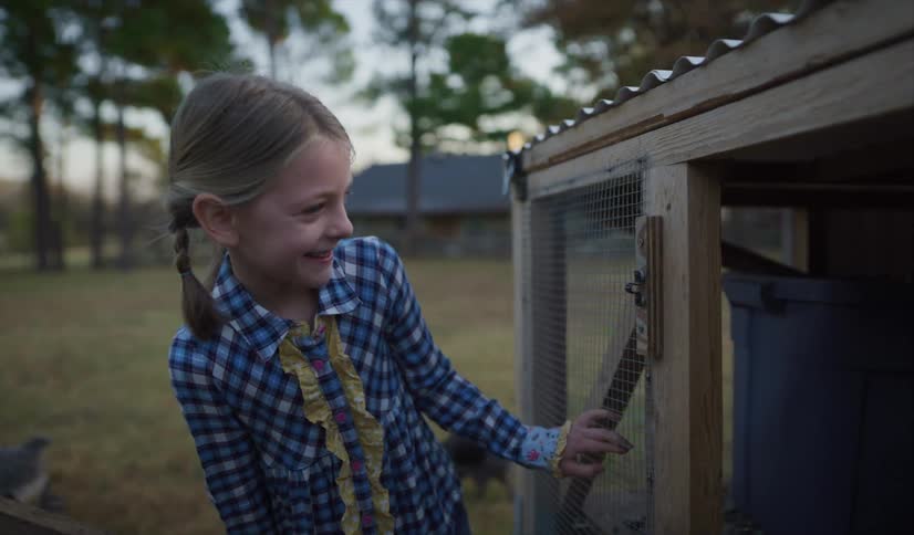 Little girl laughing while looking inside a chicken coup at a farm