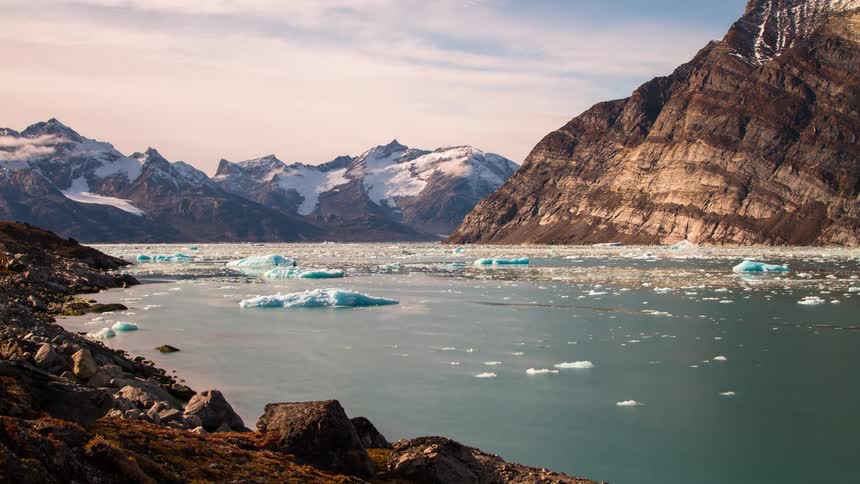 Ice is floating in a lake surrounded by mountains under a cloudy sky