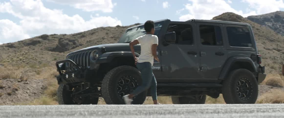 Woman stands near hills talking on mobile phone before getting back into car