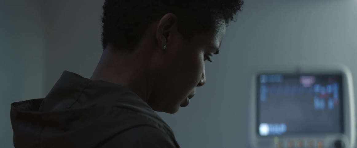 A woman stands in a hospital room as a machine runs in the background