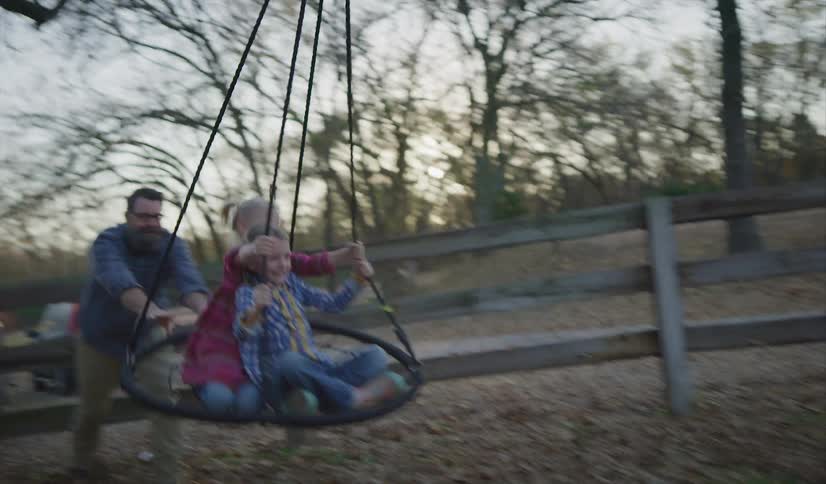 Father pushing a swing with his two daughters on it at sunset