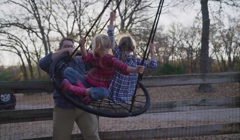 A father pushing a swing with his daughters on it in a farm