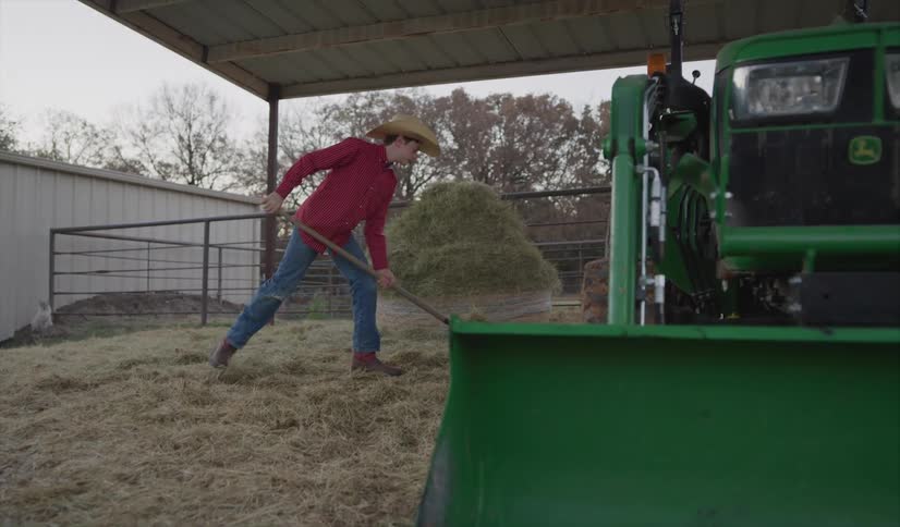 Teenage boy picking hay with a pitchfork near a green tractor