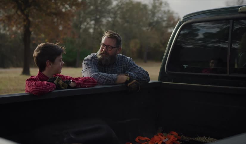 A father and son lean against a truck and talk