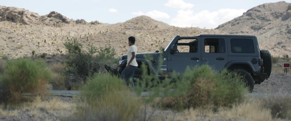 Woman talking on the phone gets out of a vehicle parked on a road in the desert
