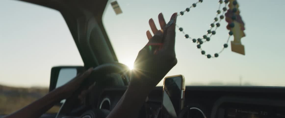 Woman holding the cross on a rosary hangin from the rearview mirror of a moving car