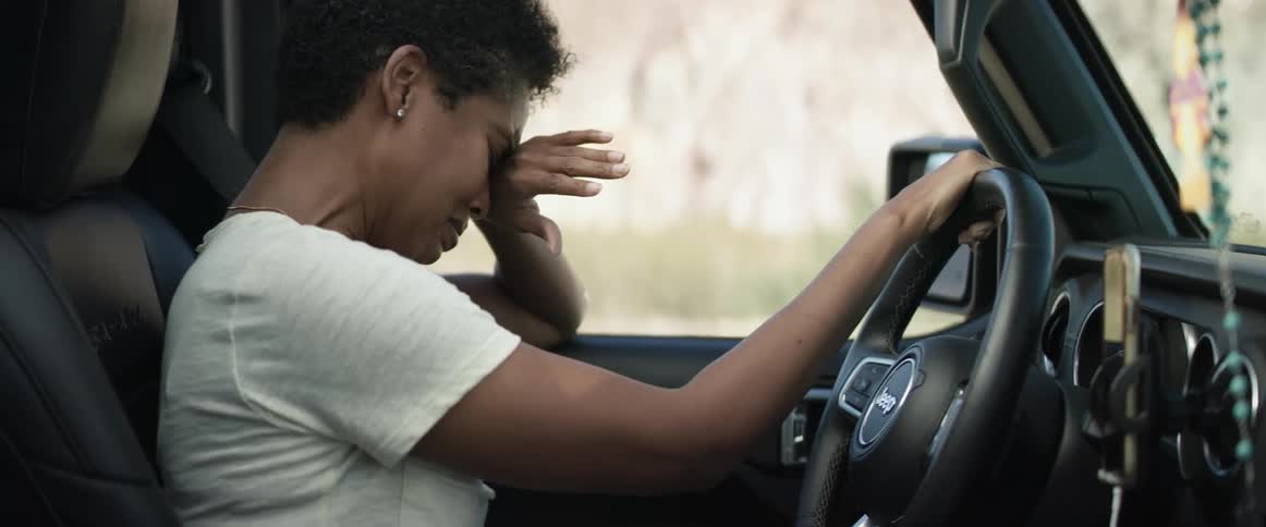 A woman in a vehicle crying with a rosary on the rearview mirror