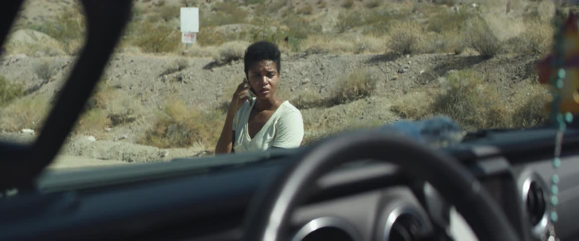Nervous woman talking on the phone near a car parked in the desert