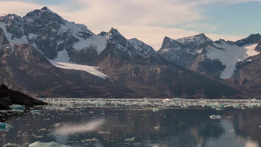 Chunks of ice flood on a lake in front of a mountain range