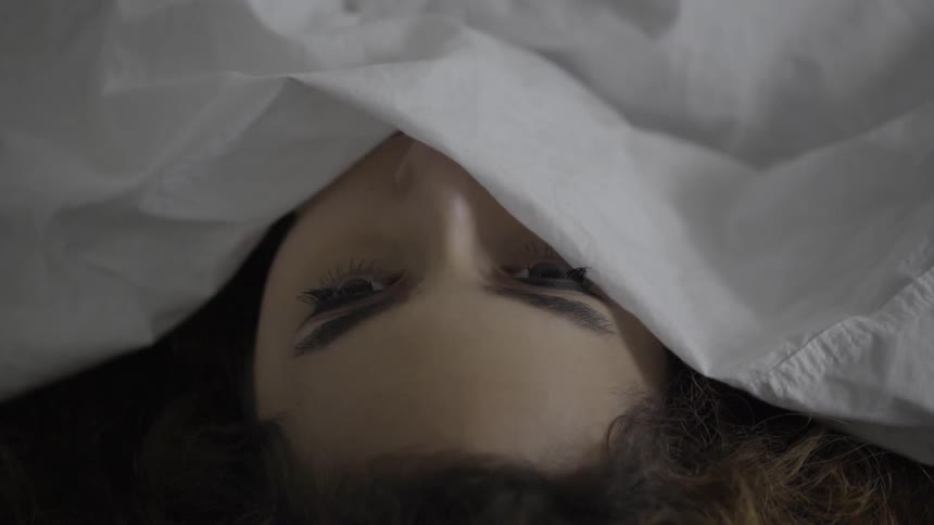 A woman looks out from underneath a bed sheet