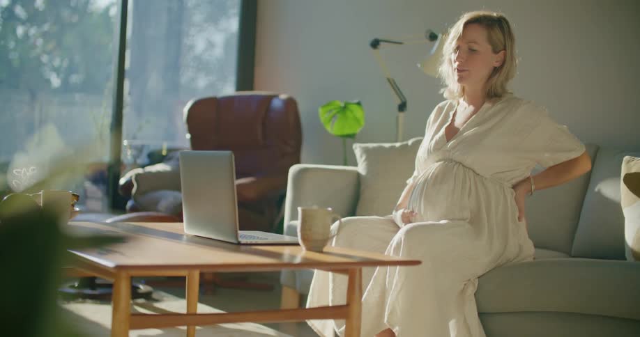 Young pregnant woman sitting in the couch at home talking on a video call on a laptop
