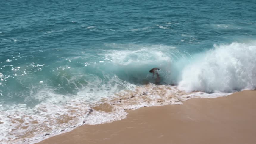 A man skimboards into the ocean and rides a wave back that crashes over him on shore