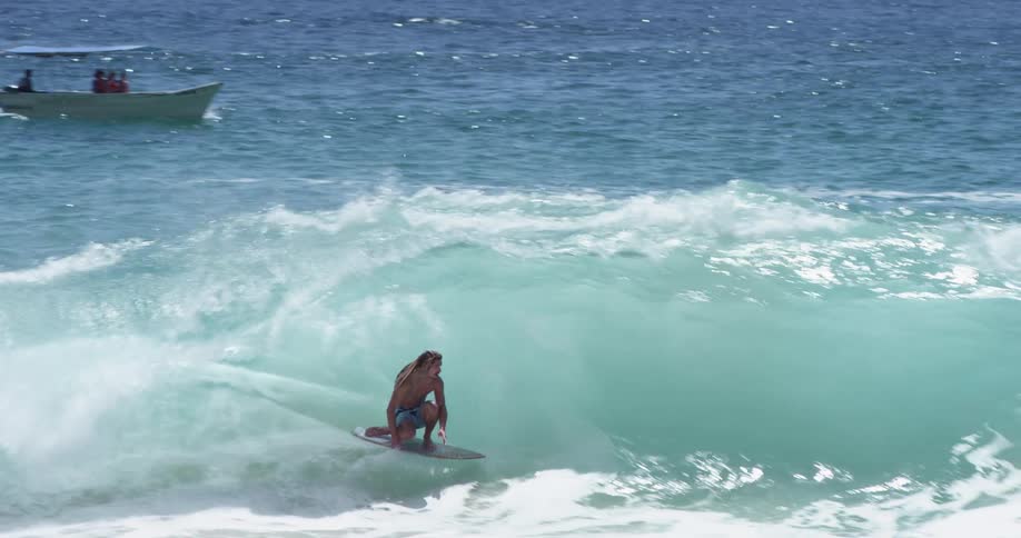 A man with dreadlocks skimboards and rides a wave to shore where it crashes over him